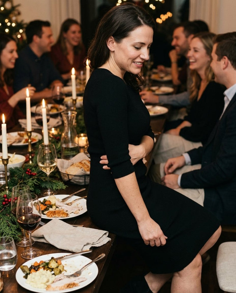 A woman at a holiday dinner sucking in her stomach, one arm folded across her belly while the others eat freely